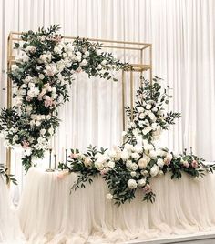an arrangement of white flowers and greenery on a wedding ceremony arch with sheer drapes