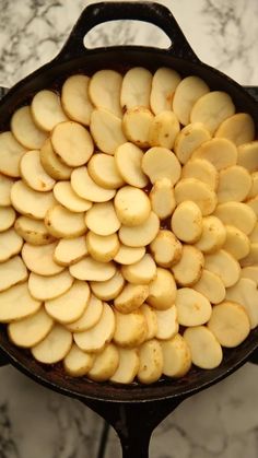 a pan filled with sliced potatoes on top of a counter next to a person's hand