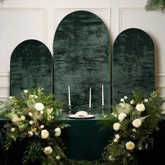 two green chairs with white flowers and candles on them in front of an arch decorated with greenery