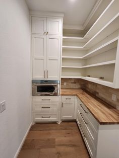 an empty kitchen with white cabinets and wood counter tops