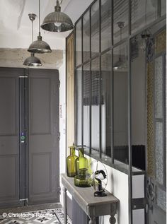 the hallway is decorated in gray and white with an antique style console table, two large glass doors, and three pendant lights