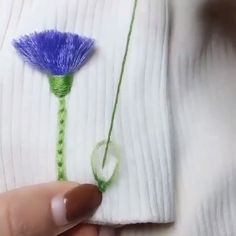someone is stitching a blue flower on a white piece of cloth with green thread