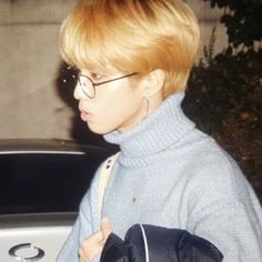 a woman with blonde hair wearing glasses and carrying a black backpack in front of a car