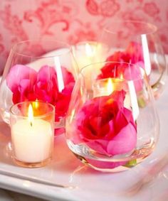 candles are lit in glass vases with pink flowers on the tray next to them