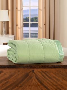 a bed with a green comforter on top of it in front of a window