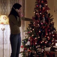 a woman standing in front of a christmas tree talking on a cell phone while holding her hand up to her face