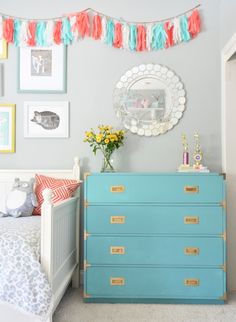 a blue dresser in a bedroom with pictures on the wall and decorations hanging above it