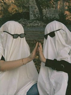 two people dressed in nun costumes sitting on the ground with their hands together and wearing sunglasses