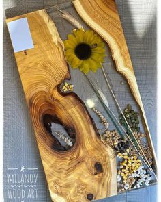 a wooden board with flowers and other items on it, including a sunflower in the center
