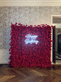 a happy birthday sign made out of red roses in a room with wallpaper and wood flooring