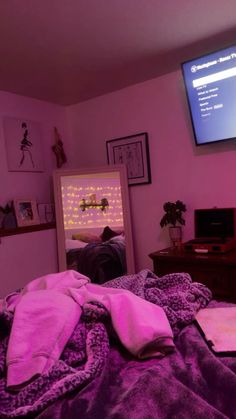 a bed with purple sheets and blankets in front of a flat screen tv mounted on the wall