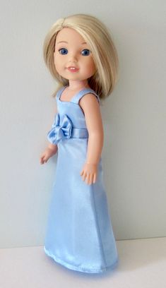 a doll with blonde hair and blue dress standing on a white counter top next to a wall