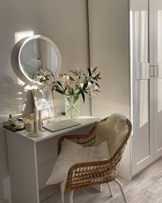 a white desk and chair with flowers in a vase on top of it next to a mirror