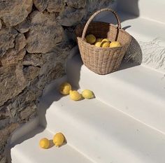 some lemons are sitting on the steps next to a wicker basket and stone wall