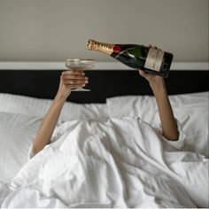 a woman laying in bed with two champagne flutes and a bottle of wine on her hand