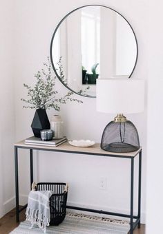 a table with a mirror, lamp and vase on it in front of a white wall
