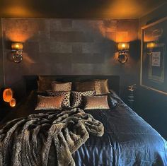 a bed with pillows, blankets and lights on the wall in a dark colored room