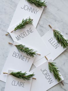 four place cards with rosemary on them sitting on a marble counter top, surrounded by greenery