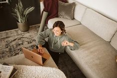 a woman sitting on the floor in front of a couch with a laptop computer open