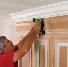 a man in red shirt using a power drill to fix a door handle on a cabinet