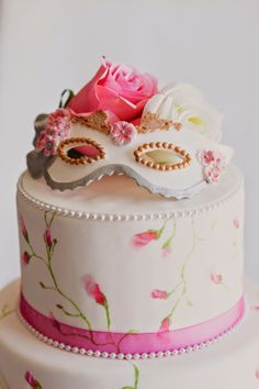 a three tiered cake decorated with pink flowers and masquerade mask on top