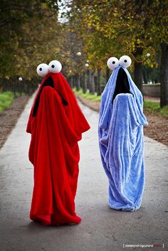 two people dressed in costumes walking down a road with eyes on their faces and mouths open
