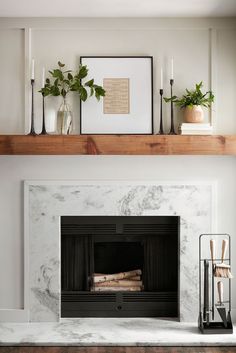 a fireplace with white marble surround and wood mantel above it is surrounded by candles