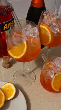 three glasses filled with orange juice and ice on a table next to two bottles of aperoli