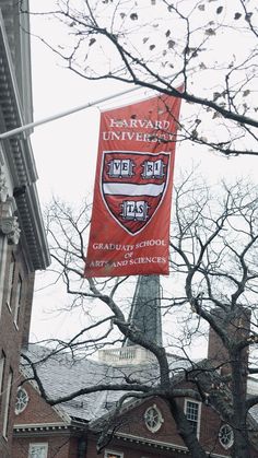 a red banner hanging from the side of a building with trees in front of it