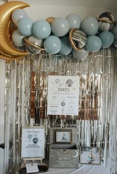 balloons are hanging from the ceiling in front of a table with silver and gold decorations