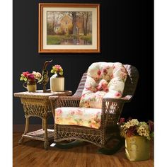 a wicker rocking chair and table with flowers on it in front of a black wall