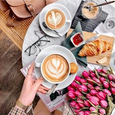 two cups of cappuccino and croissants on a table with pink tulips