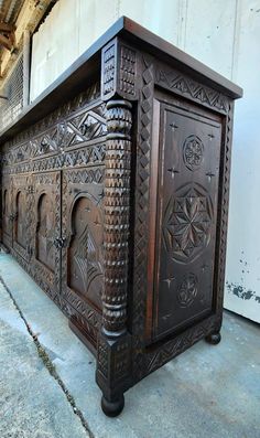 an ornately carved wooden cabinet sitting in front of a white wall and cement floor