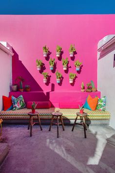 an outdoor seating area with potted plants on the wall and pink walls behind it