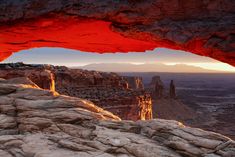 the sun is setting at the edge of a rocky cliff with red rock formations in the foreground