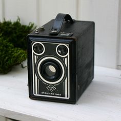 an old fashioned camera sitting on top of a white shelf next to a planter