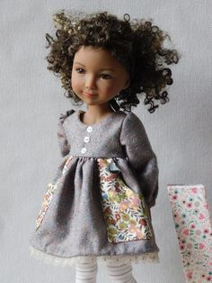 a doll with curly hair wearing a dress and tights standing next to a gift bag
