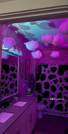 a bathroom decorated in purple and black with clouds hanging from the ceiling over the sinks