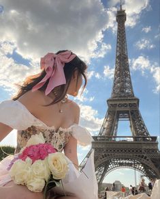 a woman sitting in front of the eiffel tower wearing a white dress and pink bow