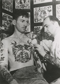 an old photo of two men with tattoos on their chest and arms, looking at each other