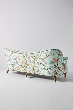 an upholstered couch with birds and flowers on the back, against a white background