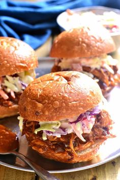 three pulled pork sliders on a plate with coleslaw slaw and pickles