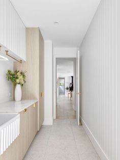 a long hallway leading to a kitchen with white walls and beige flooring on both sides