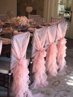 a dining room table with chairs covered in pink chiffon sashes and place settings