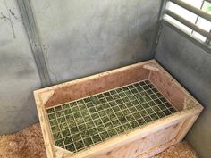a wooden box filled with grass inside of a room next to a window on the floor