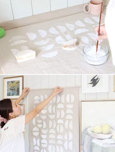 a woman is painting on the wall with white stencils, and then using a paint roller to do it