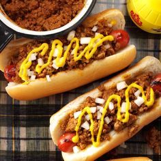two hot dogs with mustard and ketchup sitting on top of a table next to a bowl of chili