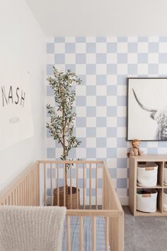 a baby's room with blue and white checkered wallpaper, a crib, and a tree in the corner