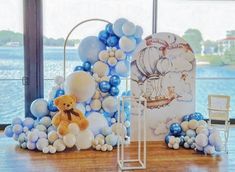 a teddy bear sitting on top of a wooden floor next to balloons and a balloon arch
