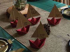 there are several small red paper boats on the table with place settings for each one